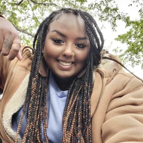 A smiling Black woman with perfect skin, dreadlocks, styled eyebrows, and a nose ring smiles at the camera.